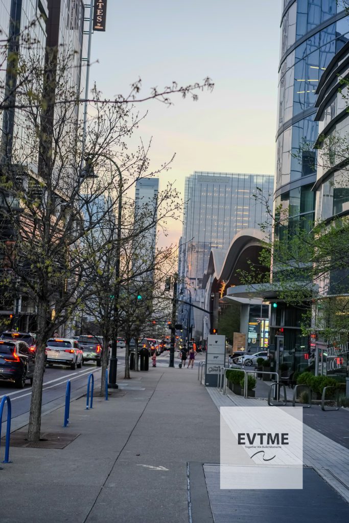 City street scene with modern glass buildings, leafless trees, and traffic at dusk; a large EVTIME ad panel is visible in the foreground on the right.